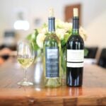Bottles of red and white Sterling Vineyards bottles and a half-filled glass on a wood table.