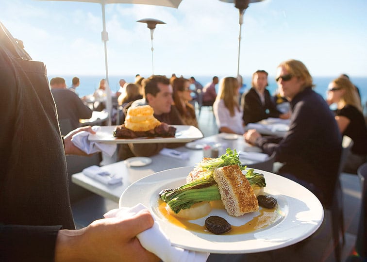 A server carries plates of food to guests at George's Ocean Terrace, which overlooks La Jolla Cove.