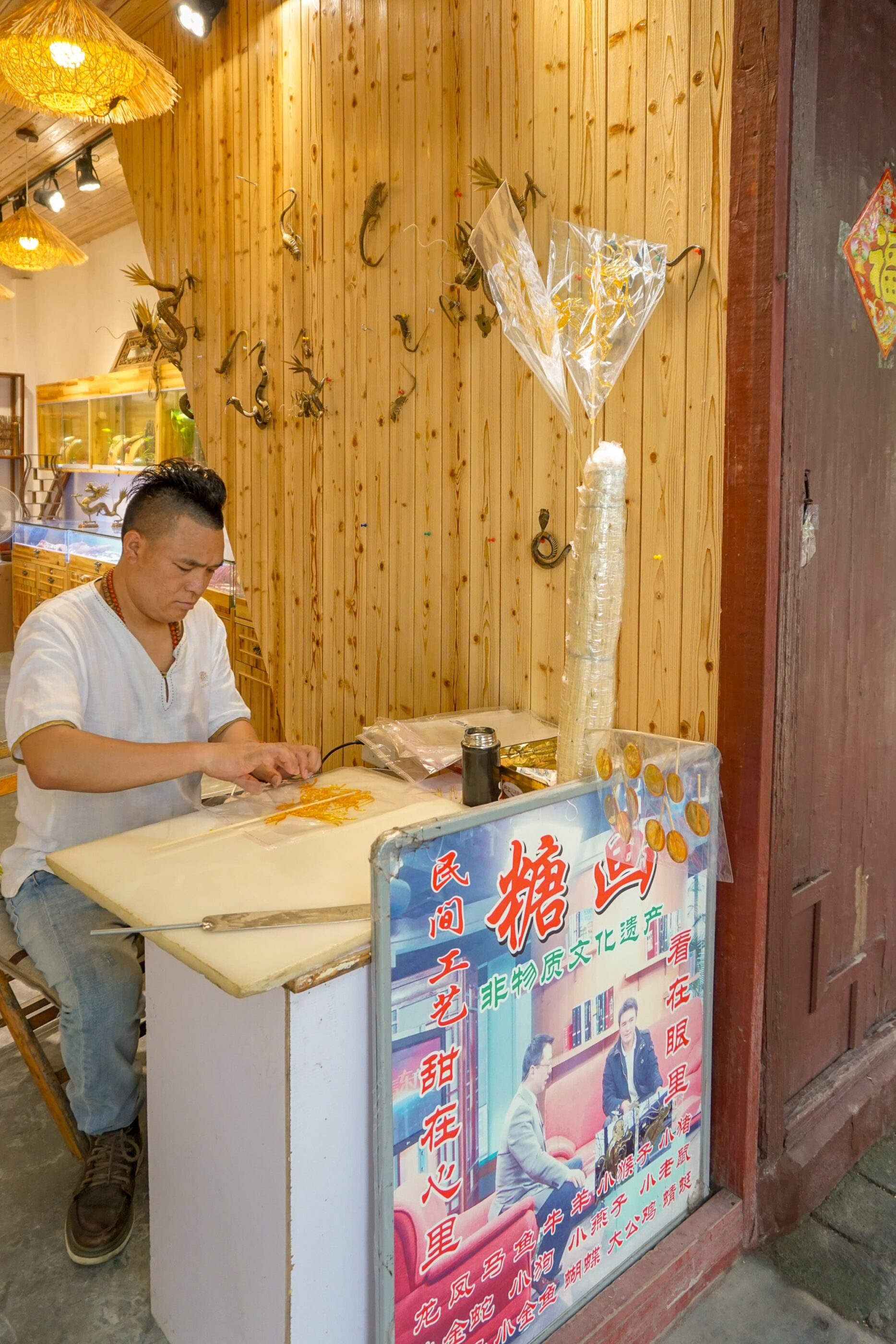 A man sits at a desk and paints animals with sugar to sell on a stick.
