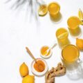 Turmeric and lemon water in cups on a white table with ginger.