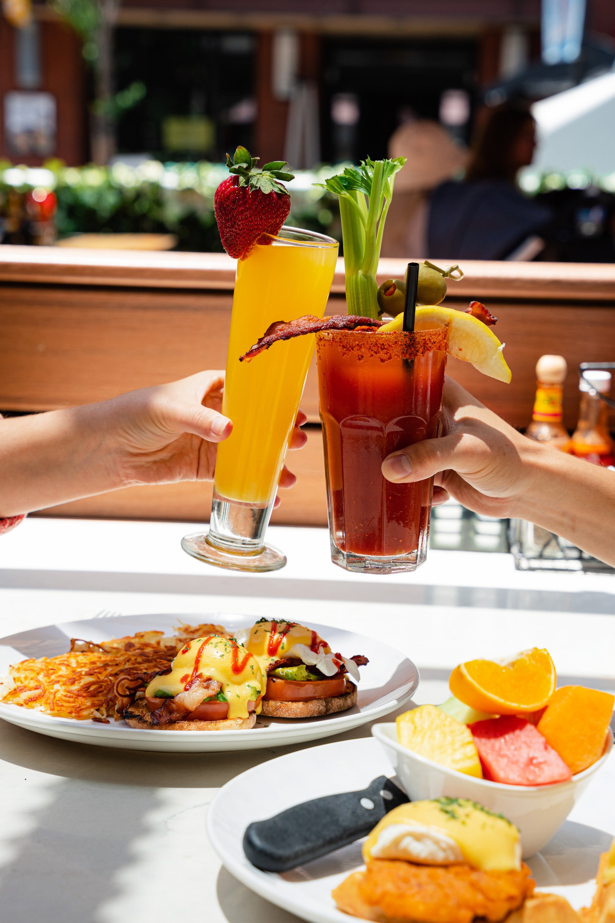 People cheers with a mimosa and Bloody Mary over breakfast Benedicts at Broken Yolk.