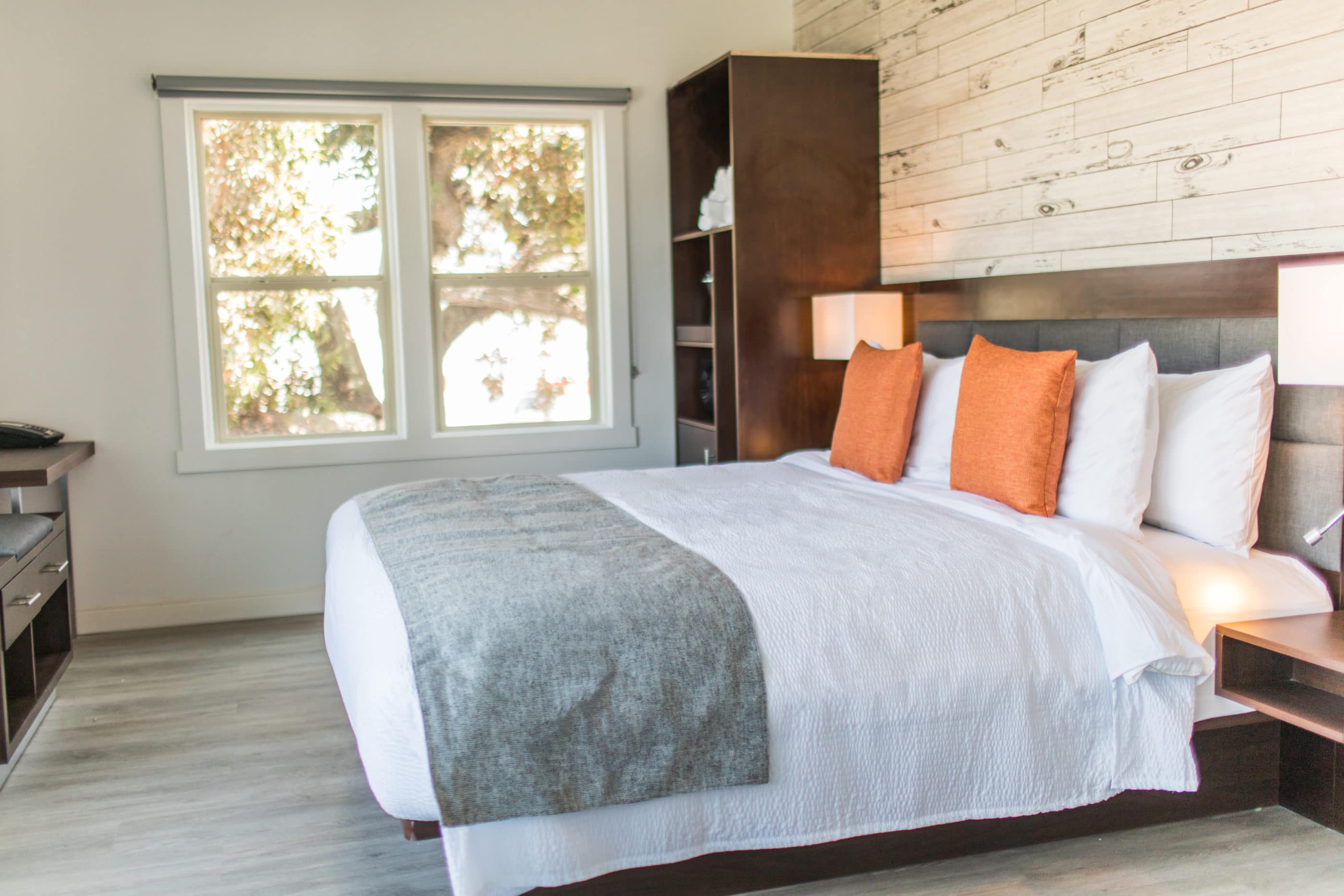 Guestroom with contemporary decor (bed with crisp white sheets, orange throw pillows and a grey blanket across the edge) at The Fin Oceanside