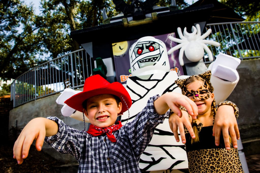 Kids in costume (cowboy and cheetah) posing next to a life-sized LEGO mummy mini figure.