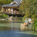 View over the water to the teahouse with a woman in a kimono walking on the terrace.