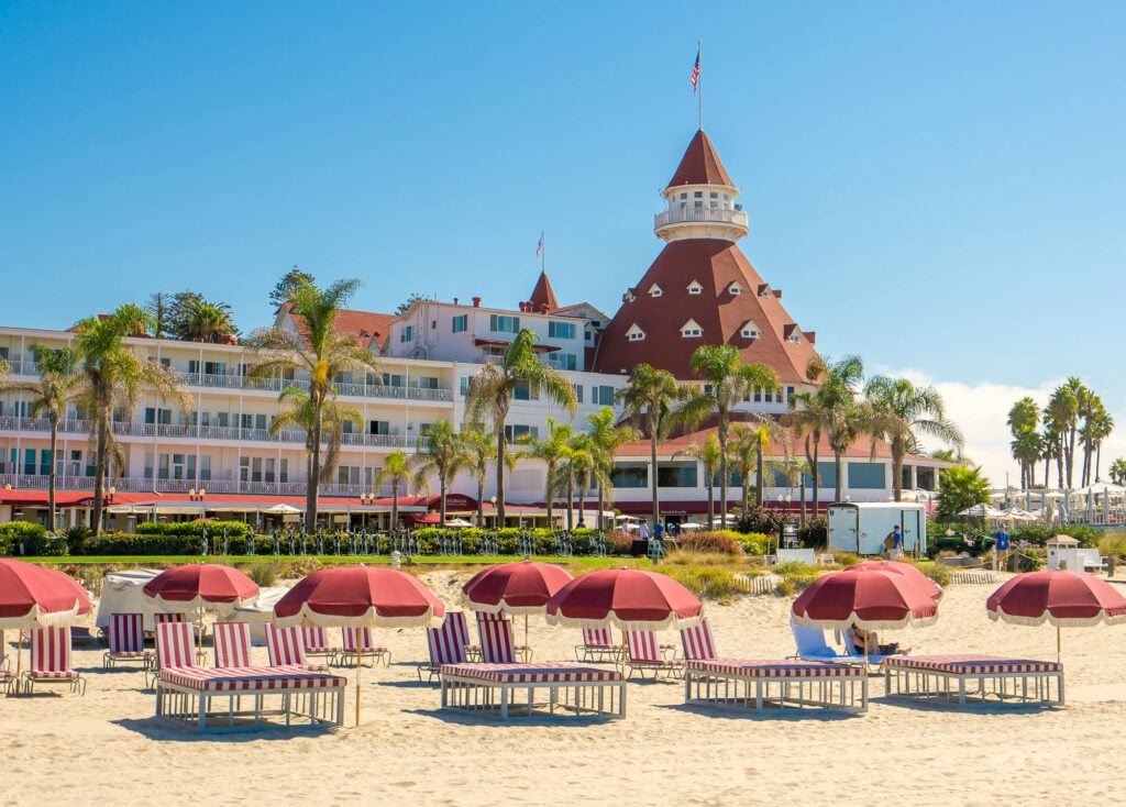 Del Beach red lounge chairs on the sand in front of the iconic Hotel del Coronado family beach resort in San Diego