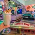 A milkshake held up in front of a vintage car at Corvette Diner in San Diego.