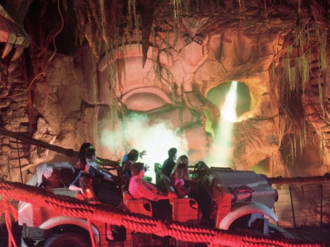 Riders in a car speed past steam and flashing lights coming from the idol of Mara in the Indiana Jones ride at Disneyland.