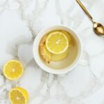 A cup of warm lemon water with ginger on a marble table.