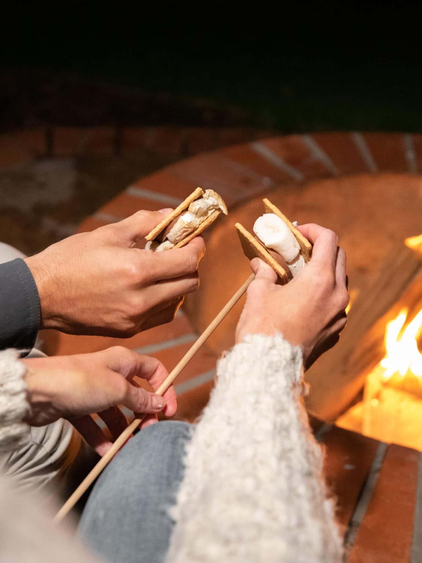 Two people roast s'mores over a hotel fire pit.