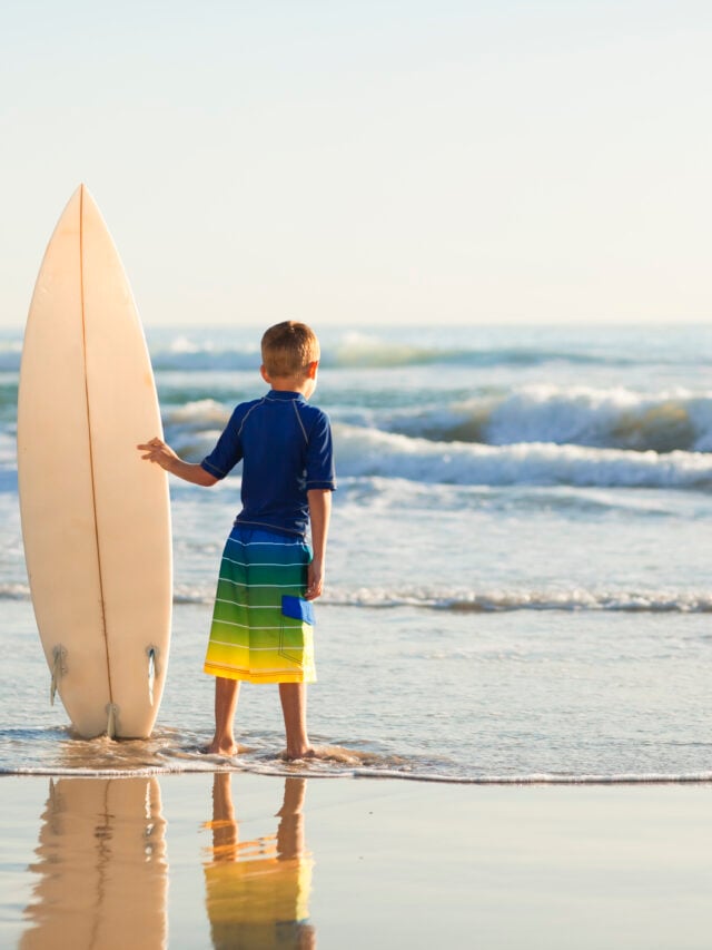 A little boy holds a surfboard on a California beach.
