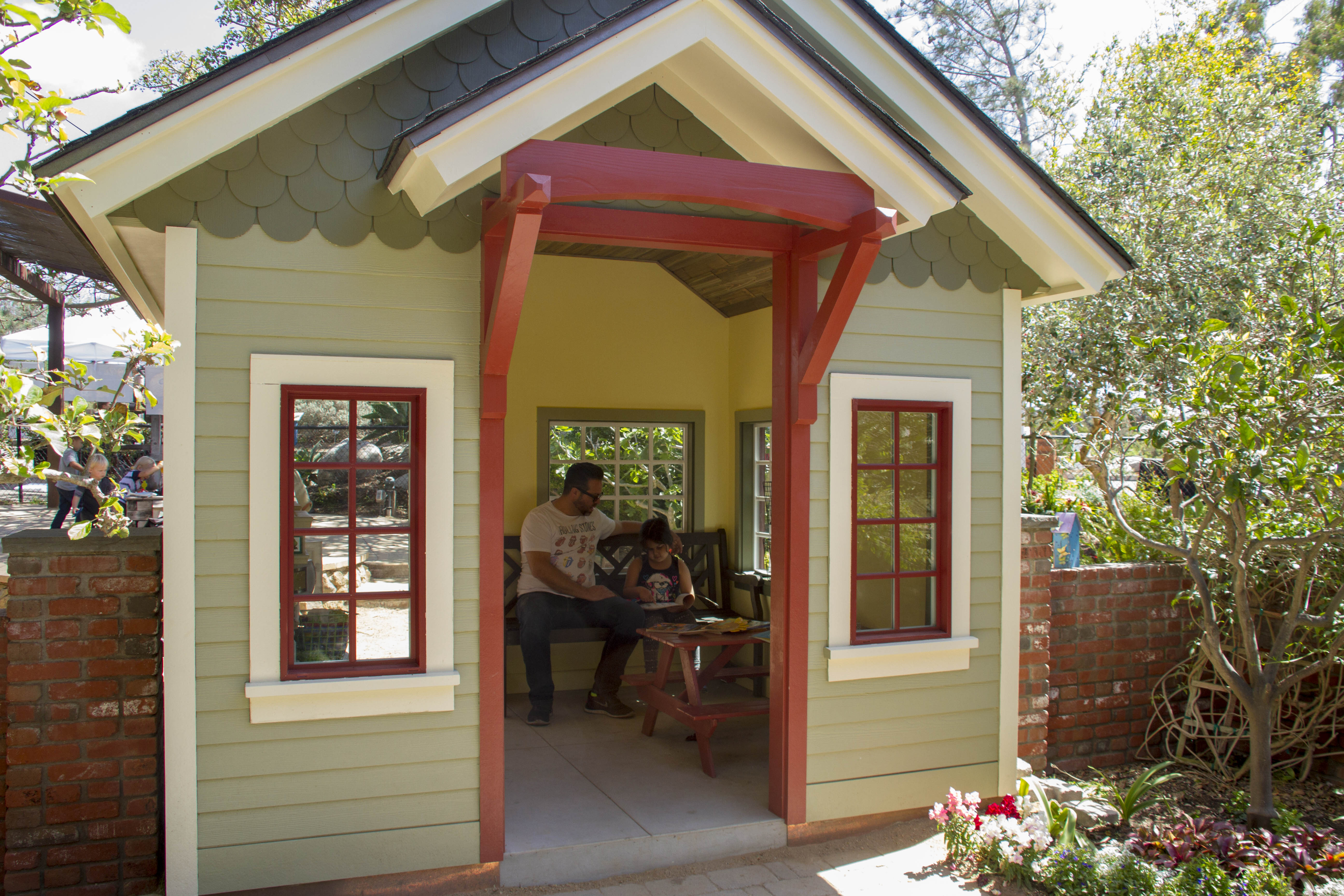 A man and girl sit on a bench inside the Seeds of Wonder playhouse.