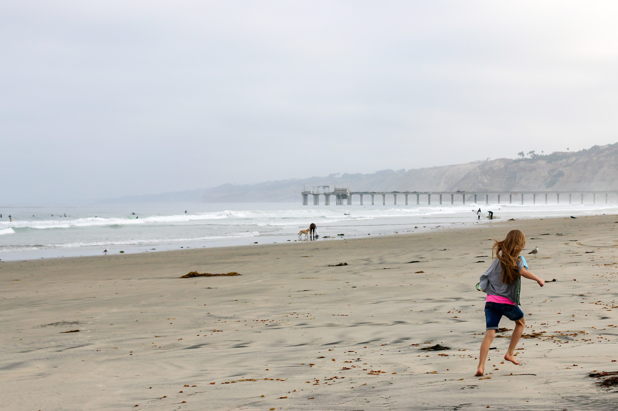 A girl runs on the sand of La Jolla Shores Beach on a cloudy morning.