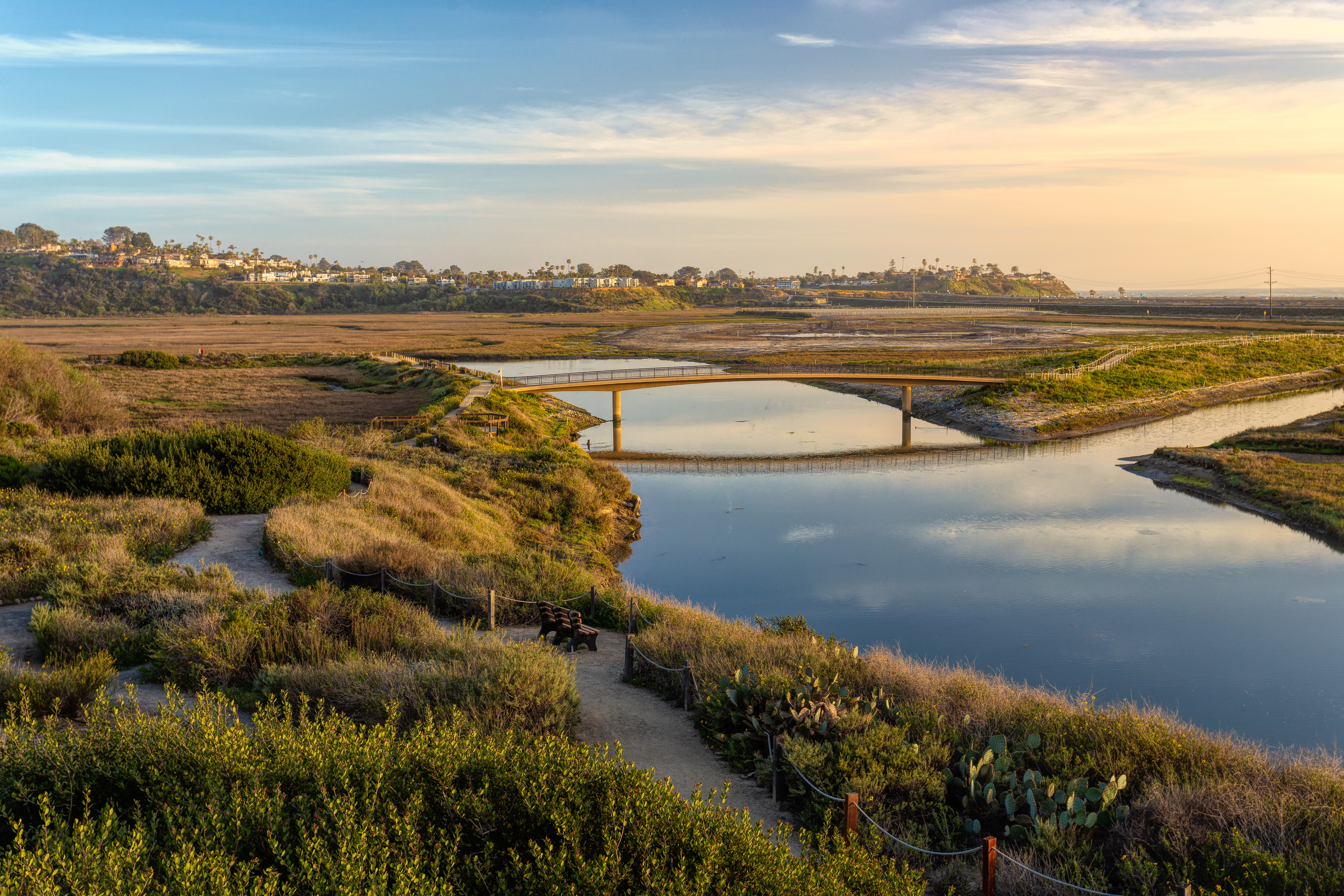 Trails with benches and a bridge crossing the lagoon at golden hour.