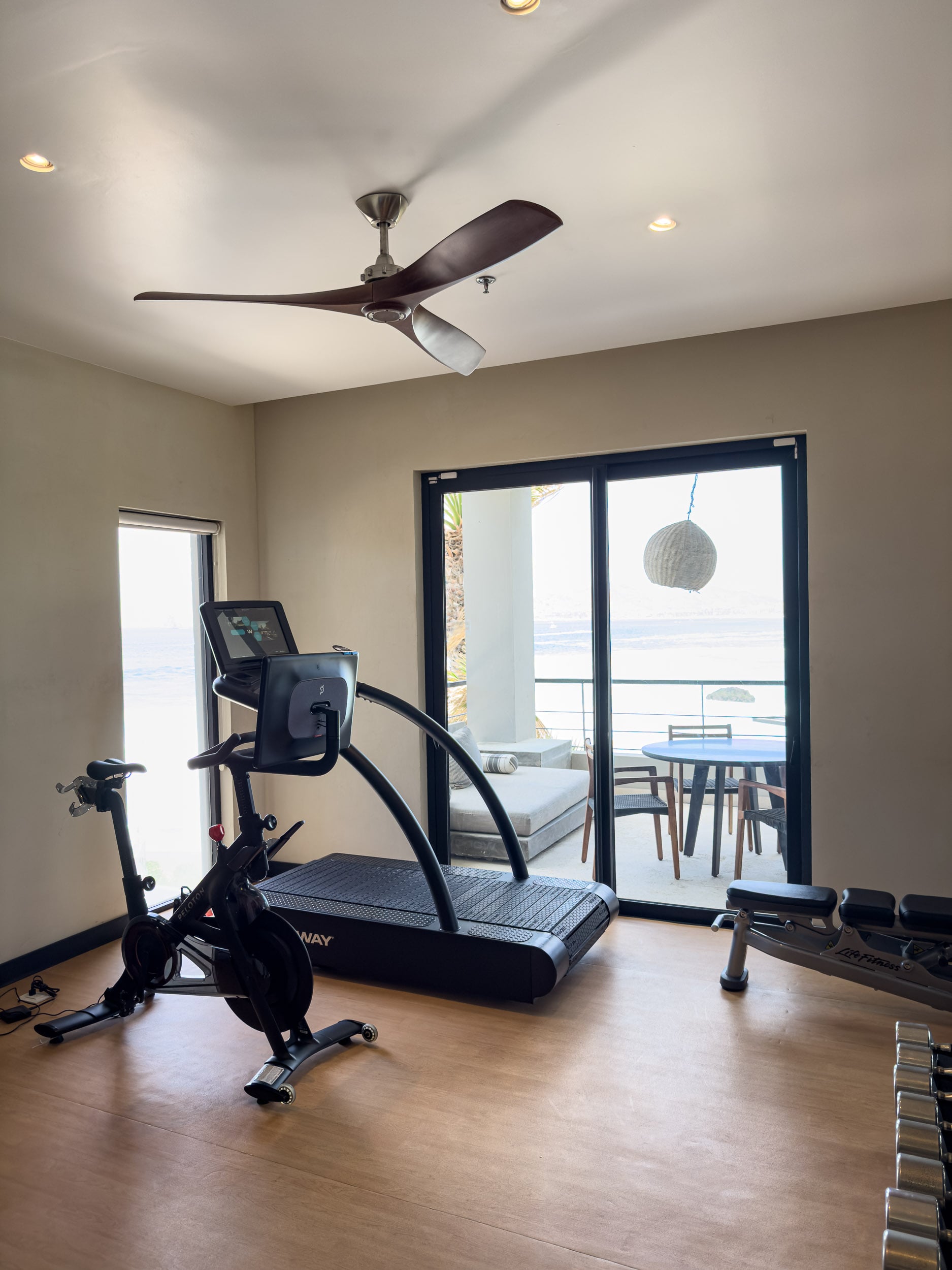 A private fitness room in a residence at The Cape, with a treadmill and exercise bike facing the terrace and ocean