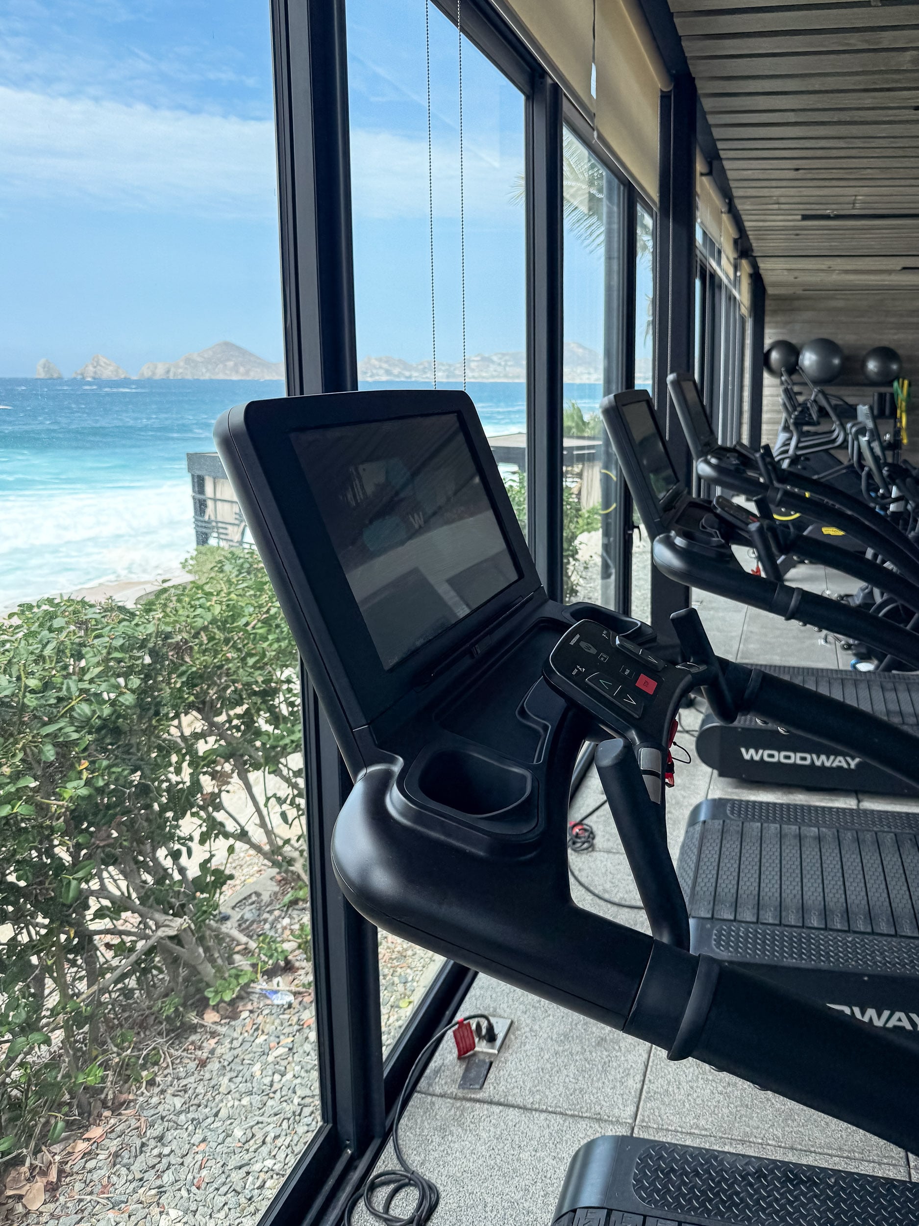 Treadmills facing floor-to-ceiling ocean views in the fitness center at The Cape, a Thompson Hotel