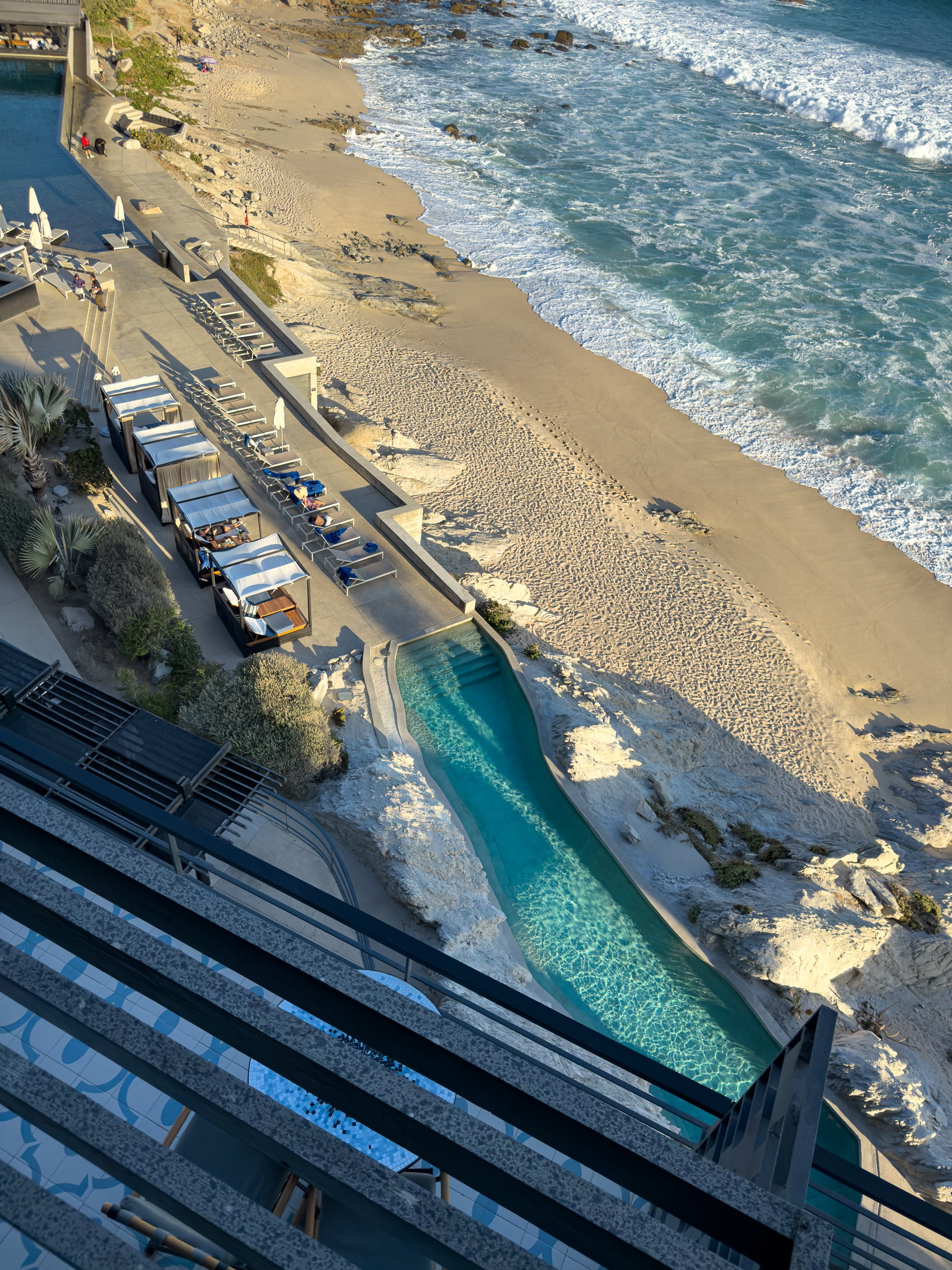 View of the oceanfront pool, cabanas, and beach from a balcony at The Cape, a Thompson Hotel