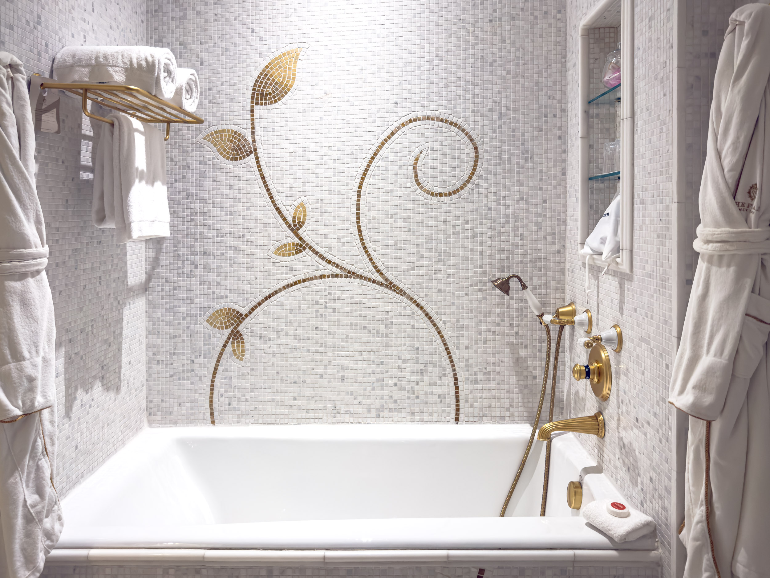 Marble bathroom with soaking tub, gold fixtures and hanging robes at The Plaza Hotel New York