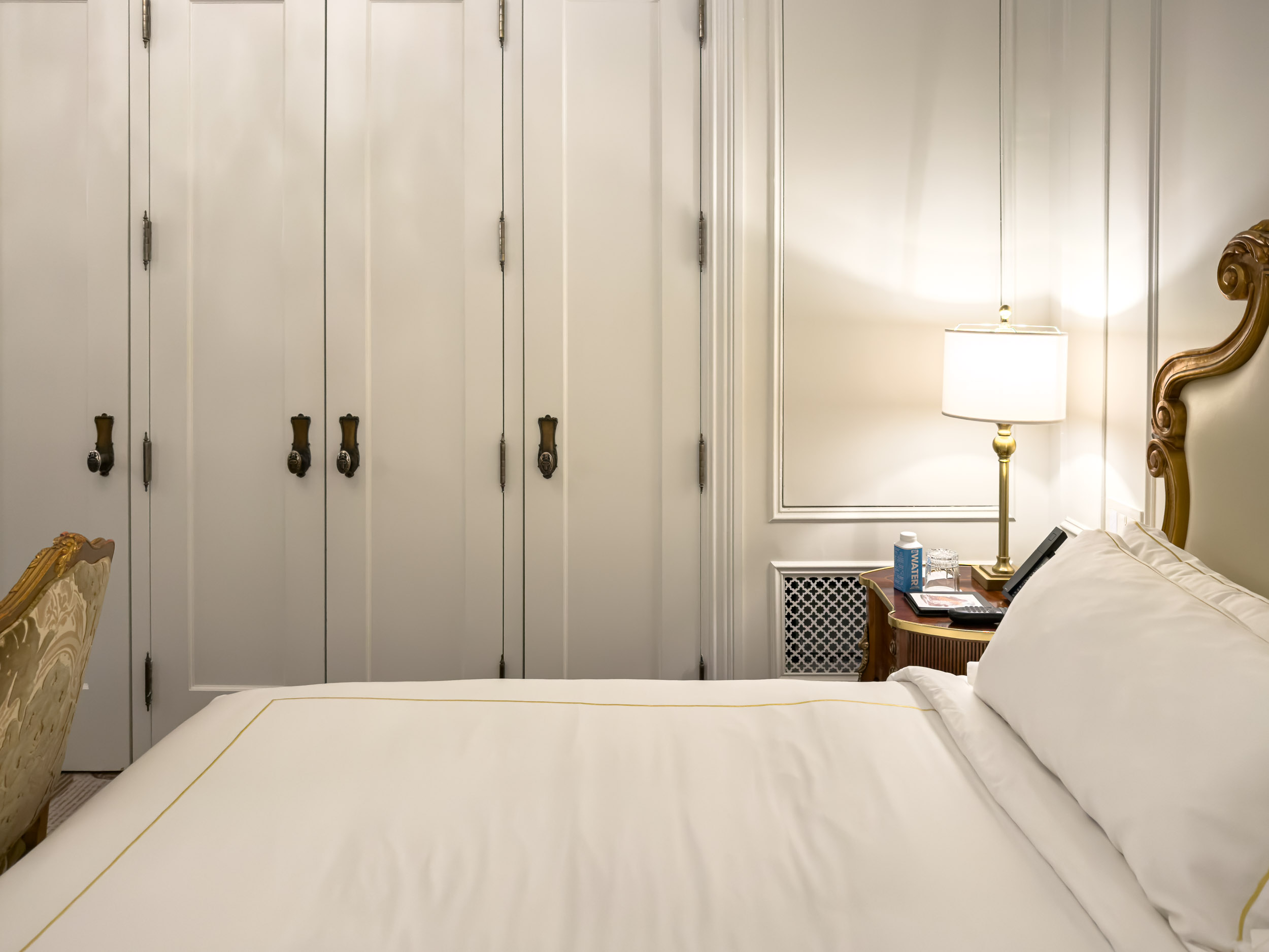 Guest room bed with white built-in closets and brass hardware at The Plaza Hotel New York