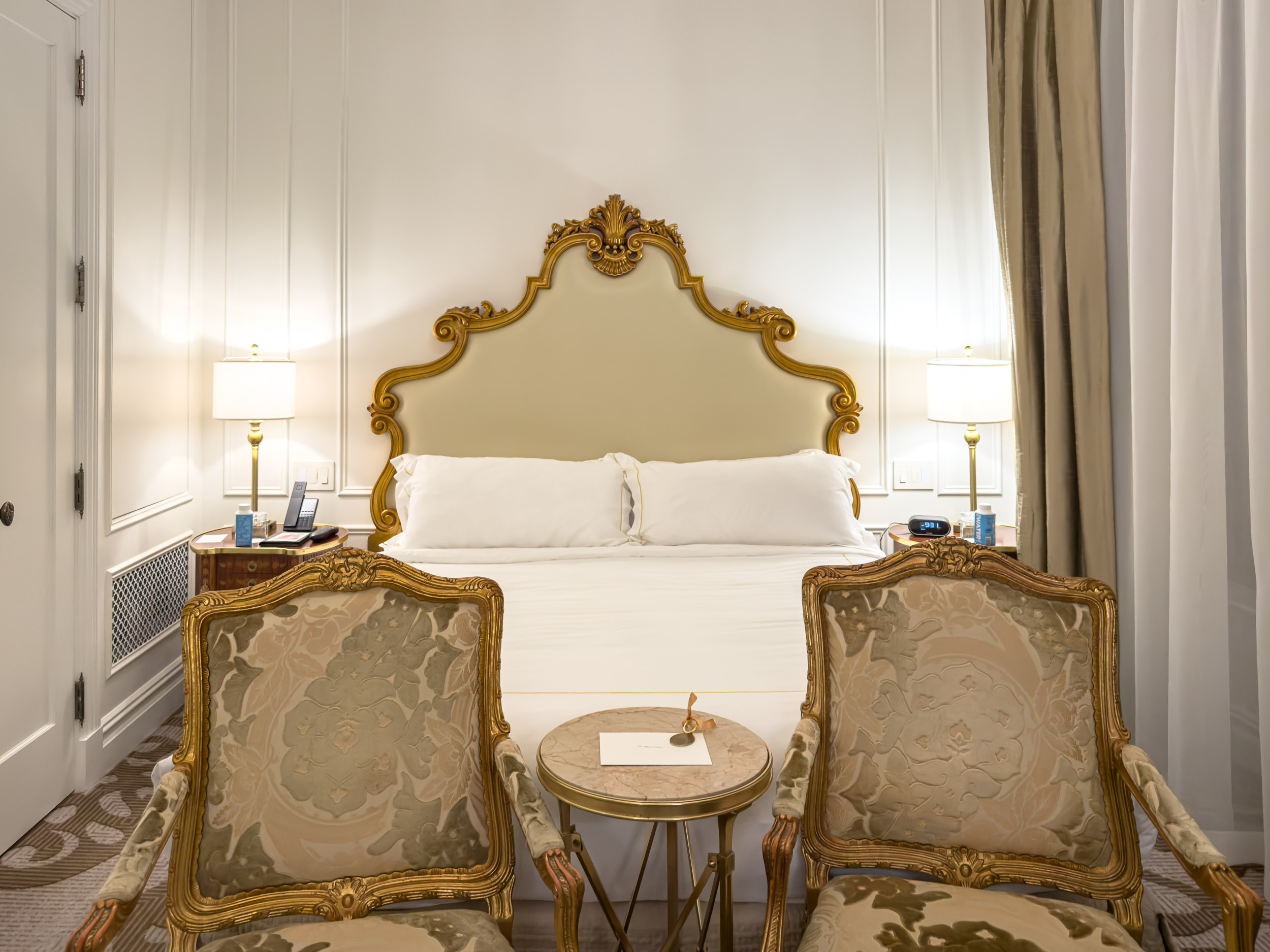Guest room bed with carved gilt headboard and gold armchairs at The Plaza Hotel New York