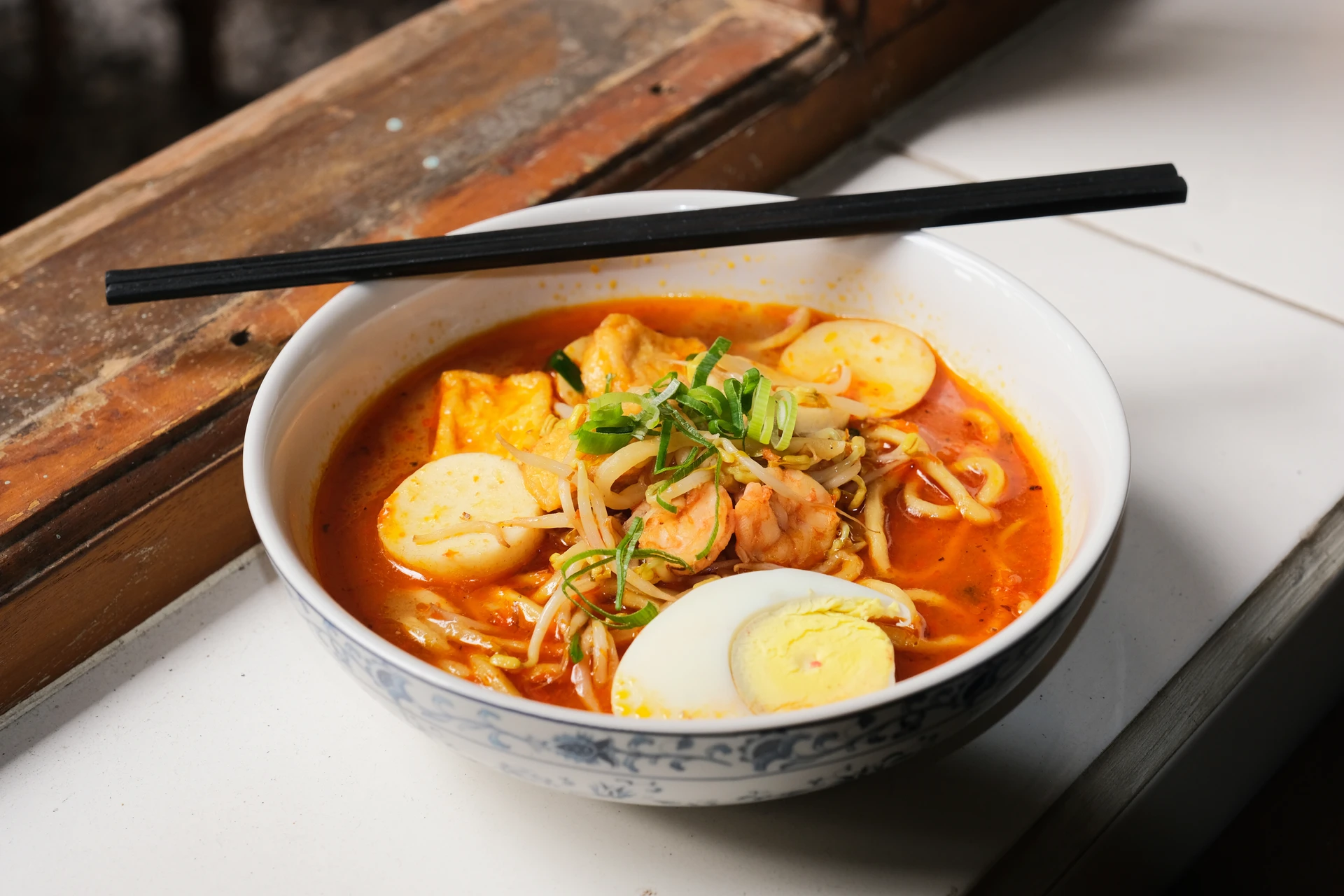 A bowl of laksa on a white countertop with shrimp and tofu puffs.