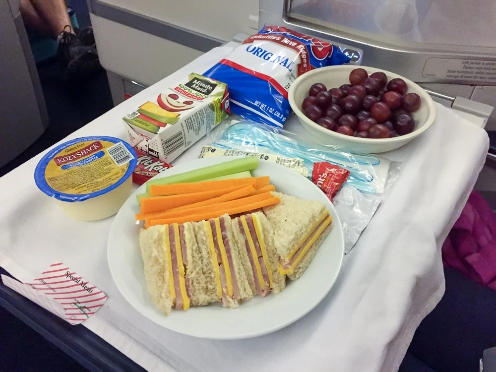 Kids' meal first course of grapes, veggie sticks, and sandwich with crusts cut off.