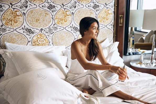 A woman sites on the bed in renovated room at Four Seasons Westlake.