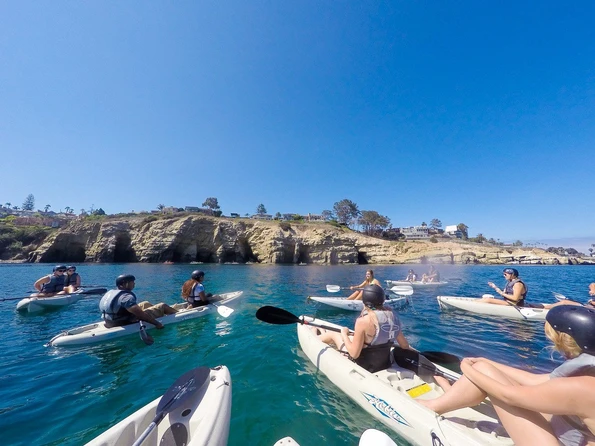 A group of kayakers on the water listening to a tour guide before taking off for the sea caves.