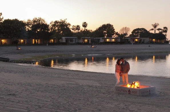 A couple stands next to a beach bonfire at sunset.