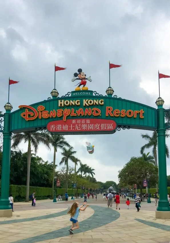 My daughter throws her Dumbo Tsum Tsum stuffed animal in the air in front of the Hong Kong Disneyland Resort sign.
