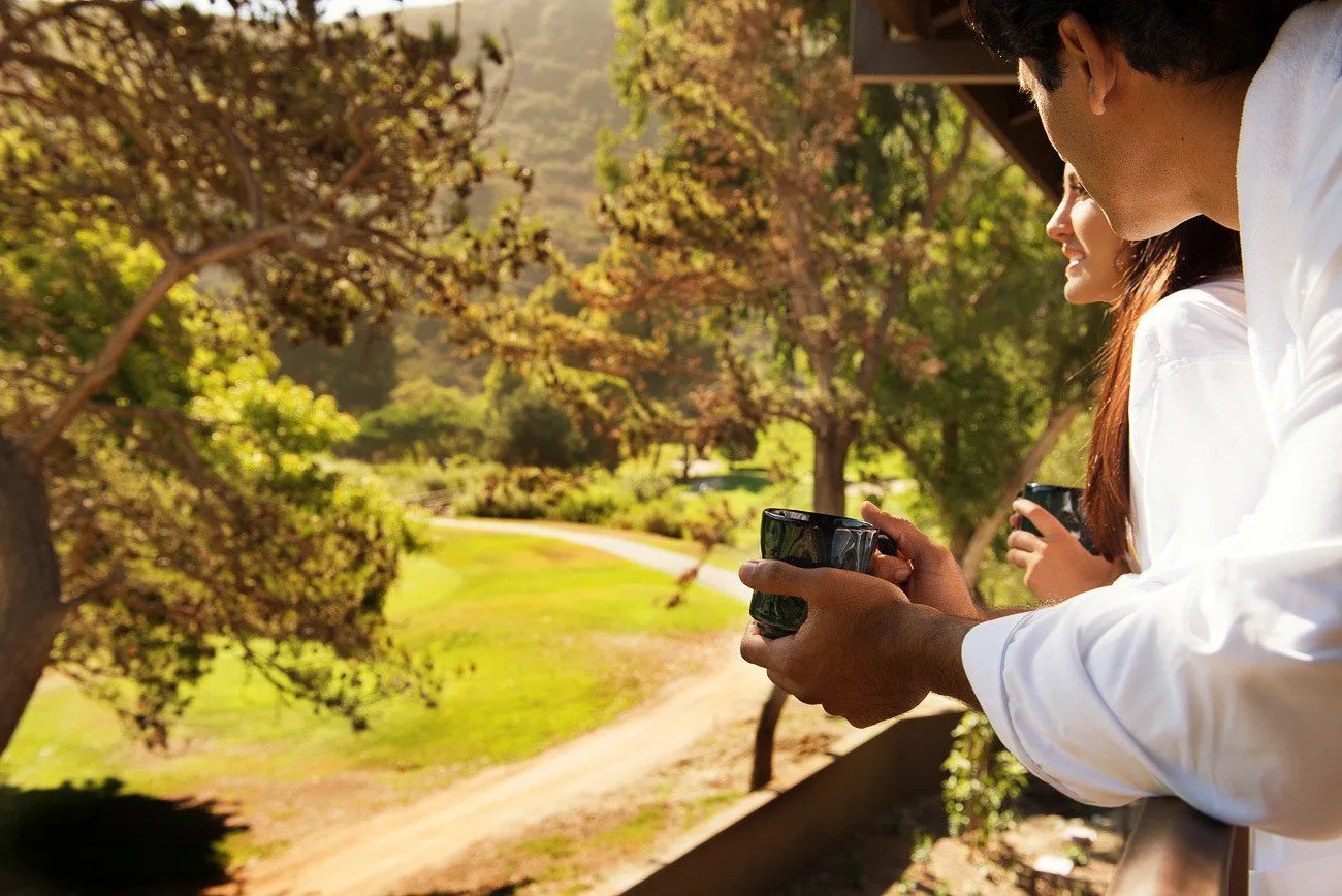 A guest holds a cup of coffee while looking at the scenery from a balcony.