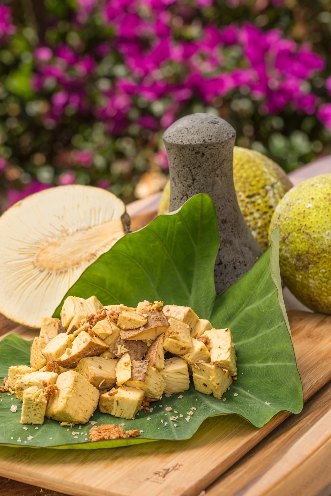 Cut breadfruit piled on a large leaf with whole fruit in the background.