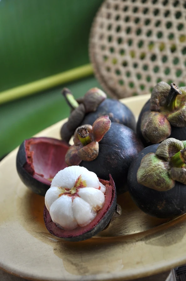 Whole mangosteen, a popular Asian fruit, on a gold plate next to one that is cut in half. 