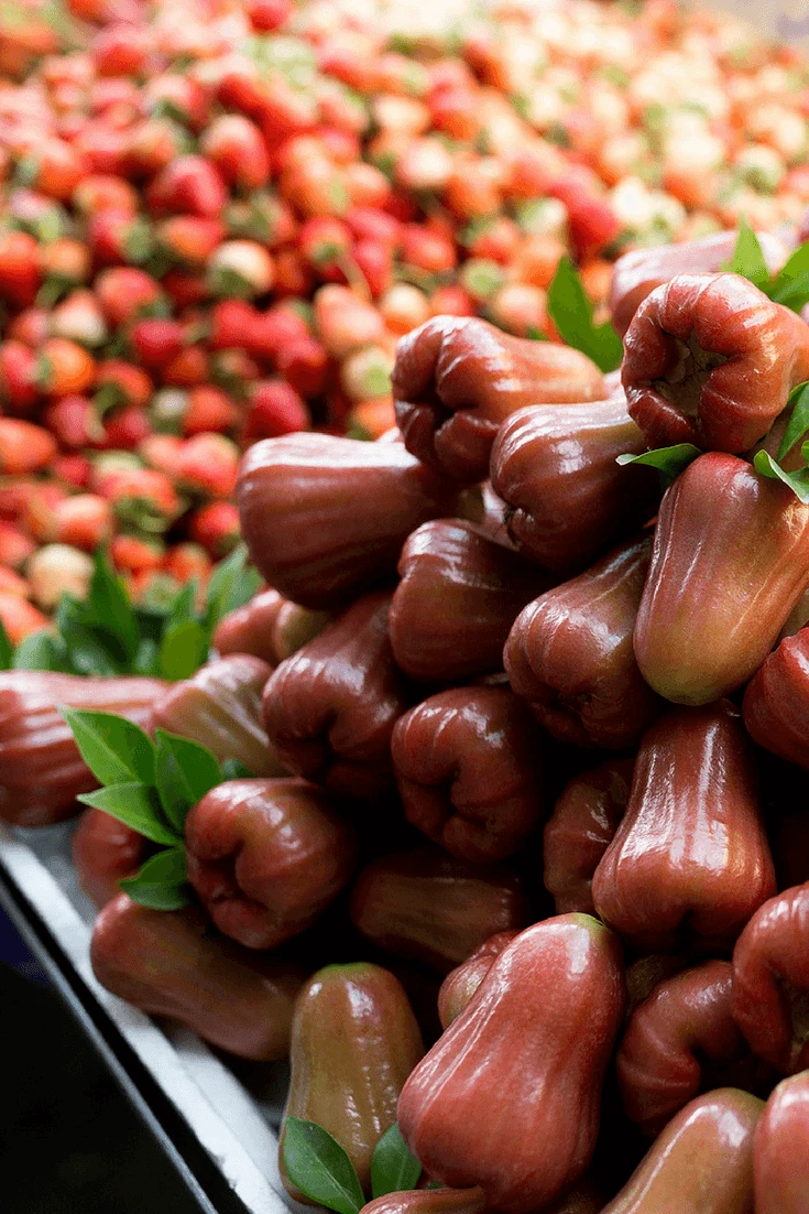 Wax applies piled up for sale at a grocery store near other exotic Asian fruit.