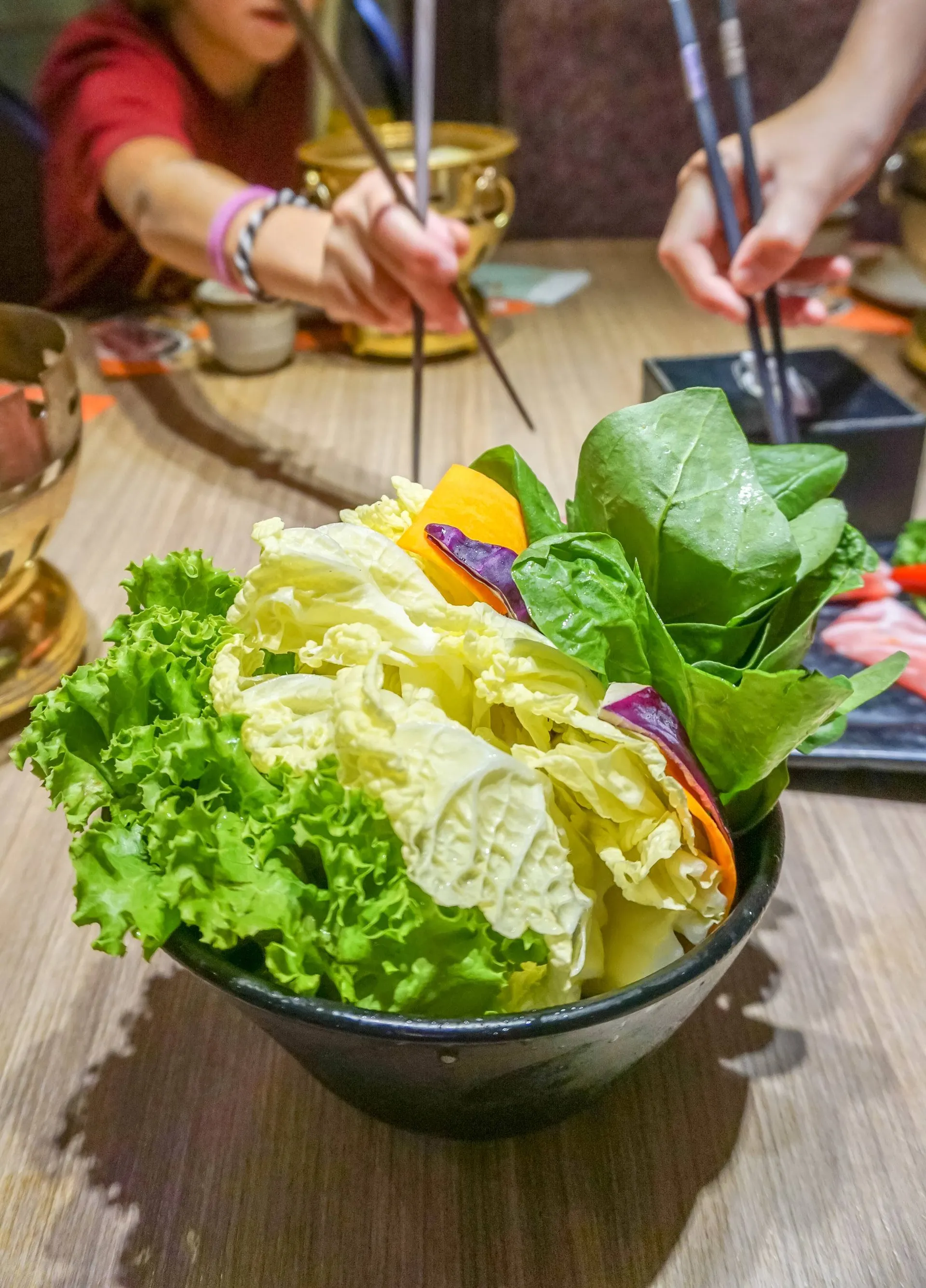 Girls reach for leafy vegetables, a common Chinese hot pot ingredient, to cook. 