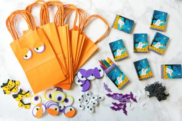 Supplies including bags, stickers and crayons to let kids decorate their own favor bags at a toddler Halloween party.