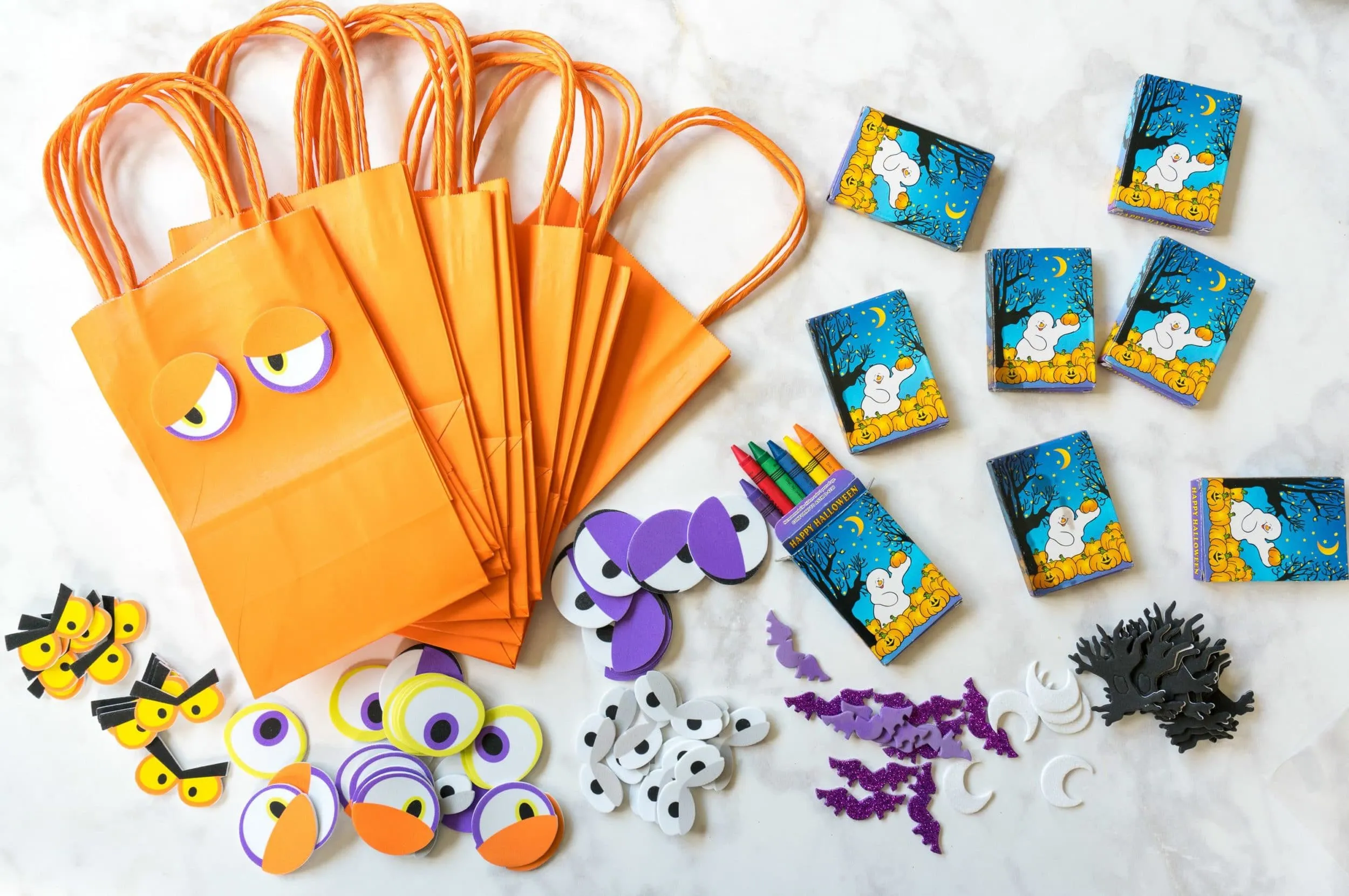 Supplies including bags, stickers and crayons to let kids decorate their own favor bags at a toddler Halloween party.