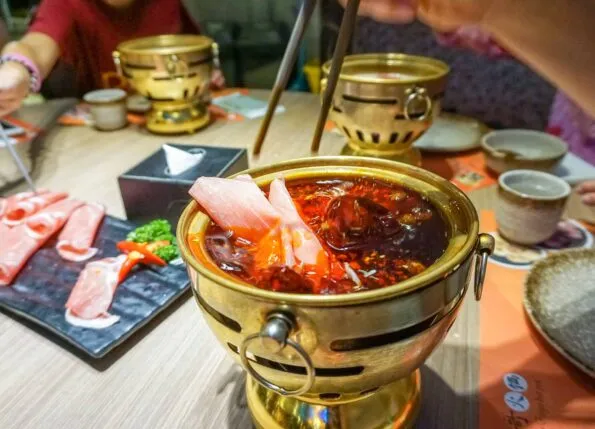 A slice of fresh meat is dropped by chopsticks into an individual Chinese hot pot.
