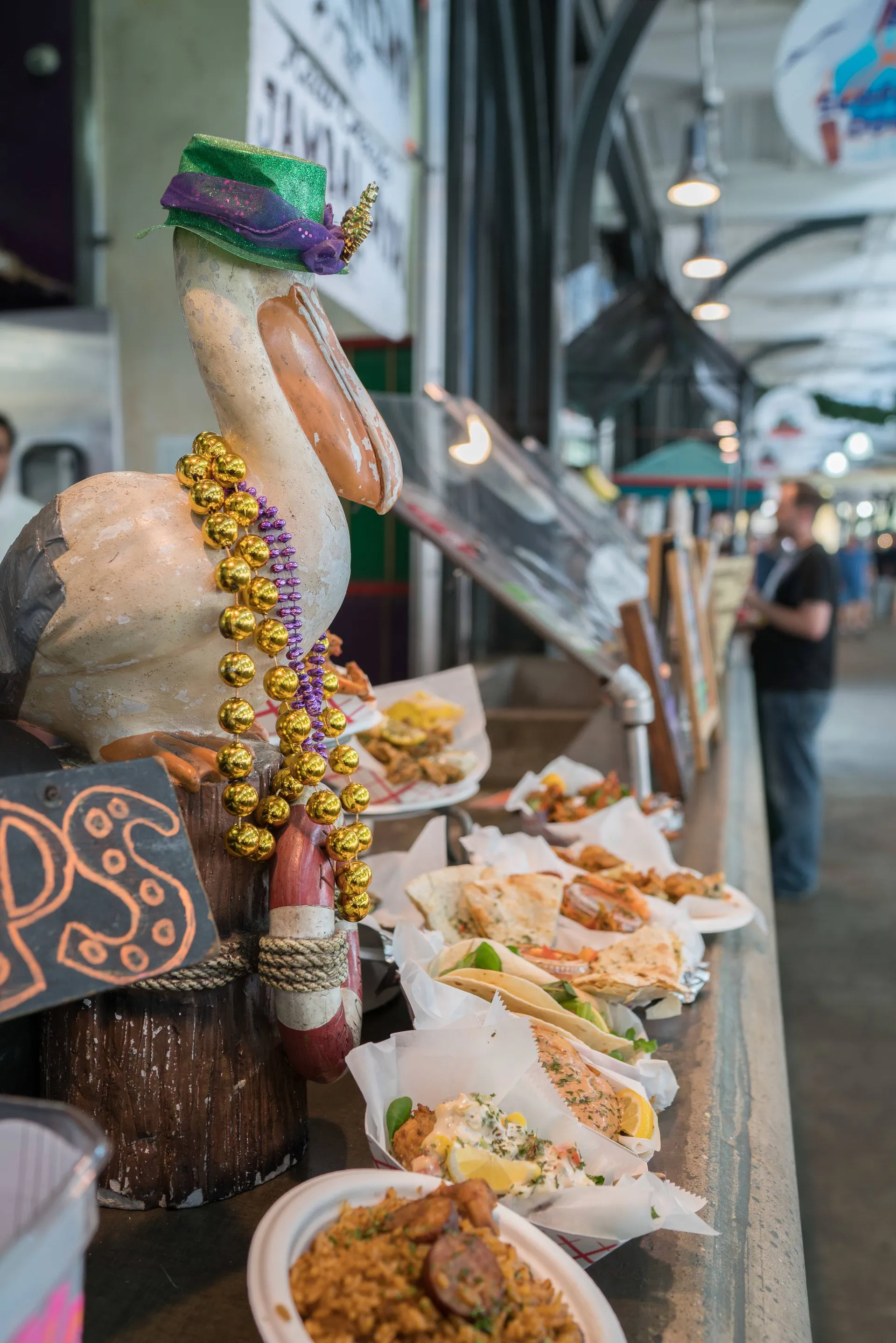 A pelican with Mardi Gras beads sits above some fried food at the French Market.