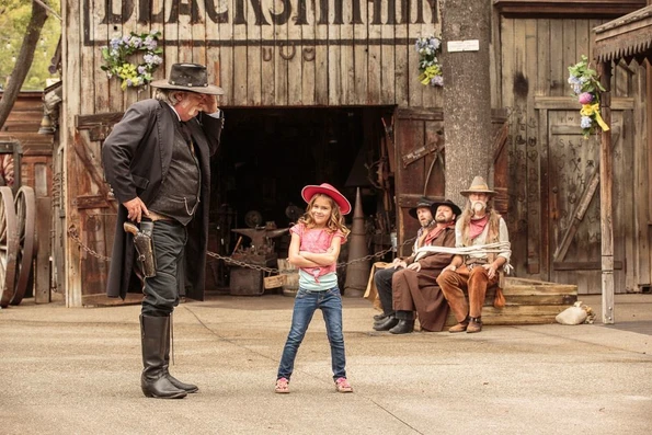 A staff member in costume in the Ghost Town role plays with a little girl in a cowboy hat at Knott's Berry Farm.