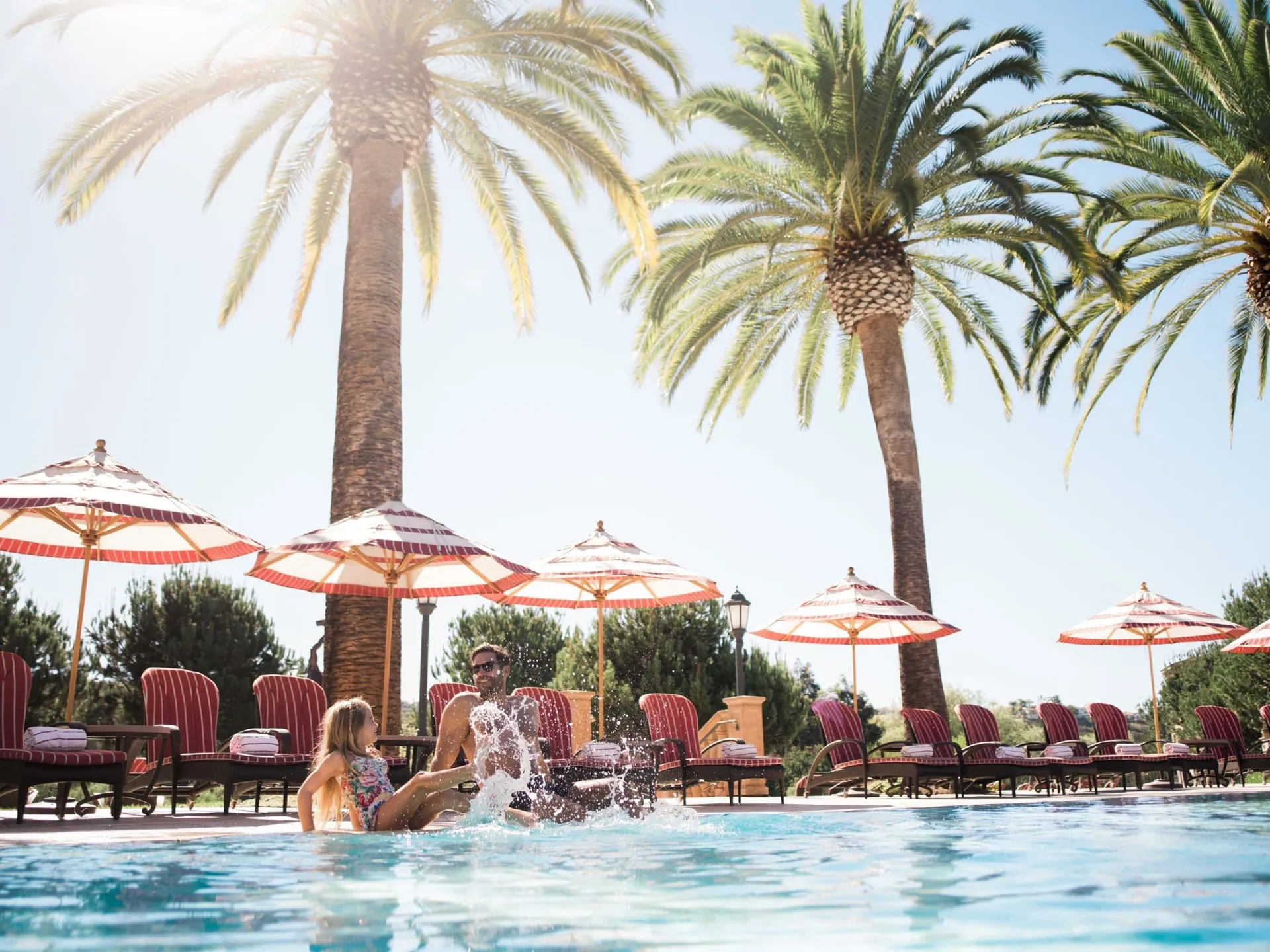 A girl splashes in the main swimming pool with her father at Fairmont Grand Del Mar, my top pick for kid-friendly hotels in San Diego.