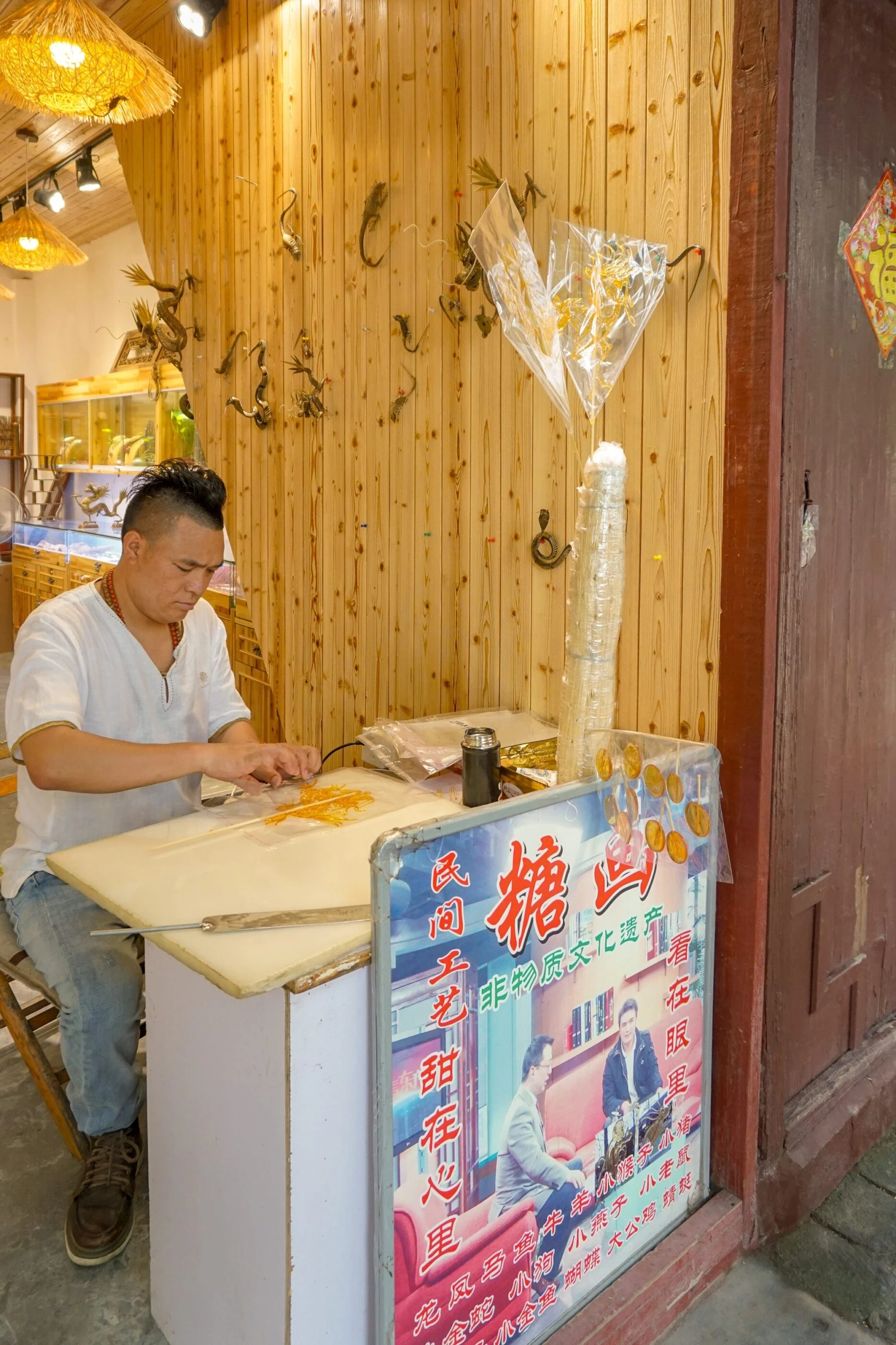 A man sits at a desk and paints animals with sugar to sell on a stick.