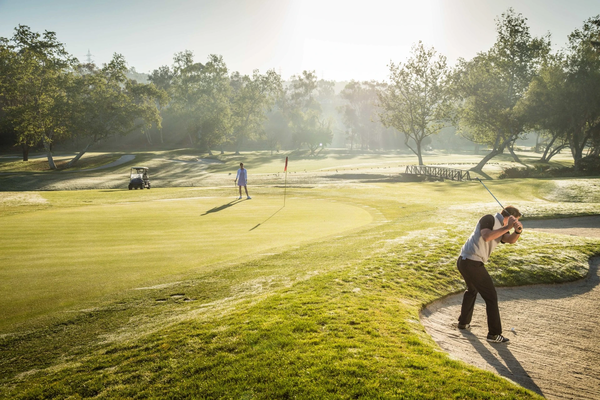 A golfer chips out of a sand trap on an Omni La Costa golf course