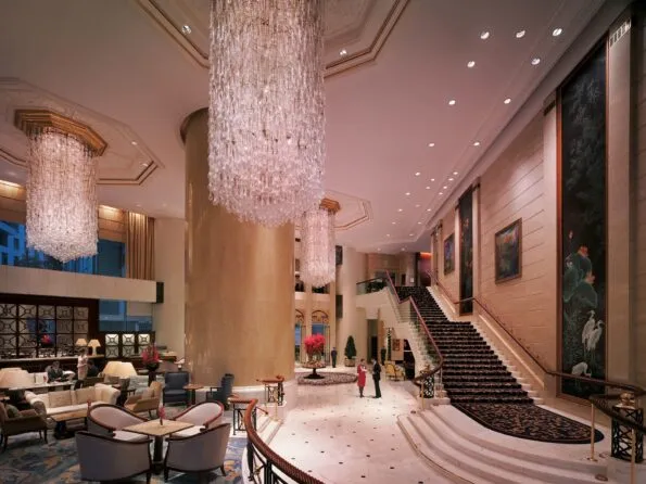 Guests walk through Island Shangri-La Hong Kong's ground floor area under large chandeliers.