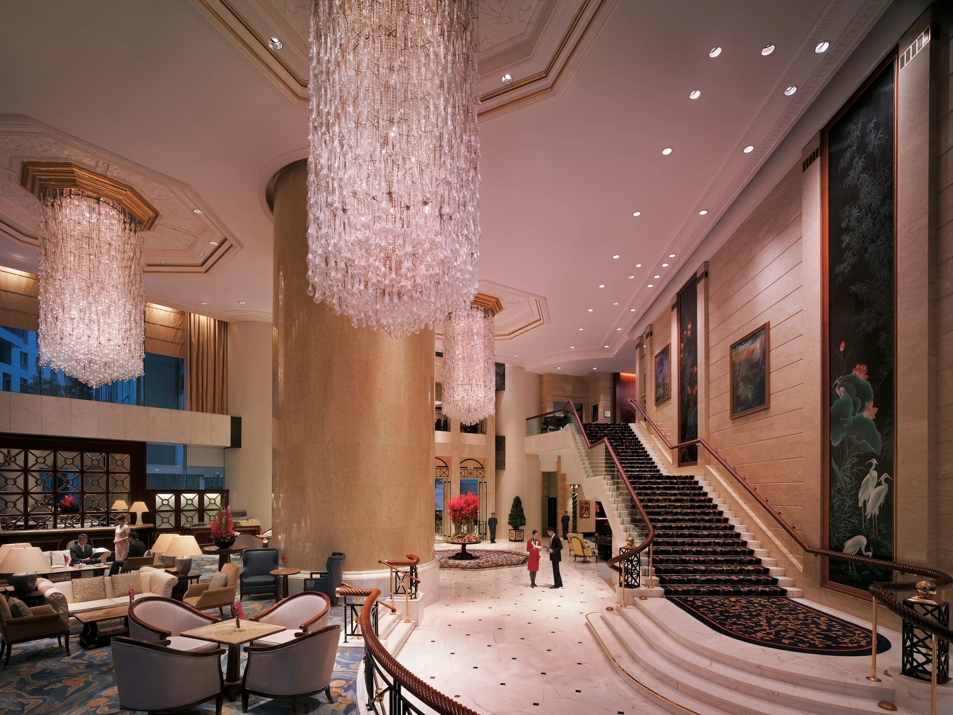 Guests walk through Island Shangri-La Hong Kong's ground floor area under large chandeliers.