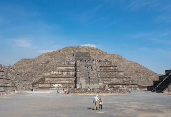 My daughter and husband walk toward a pyramid at Teotihuacan on a sunny day.