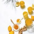 Turmeric and lemon water in cups on a white table with ginger.