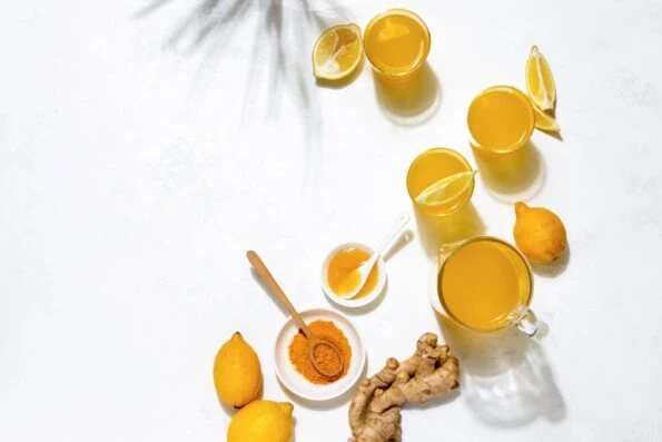 Turmeric and lemon water in cups on a white table with ginger.
