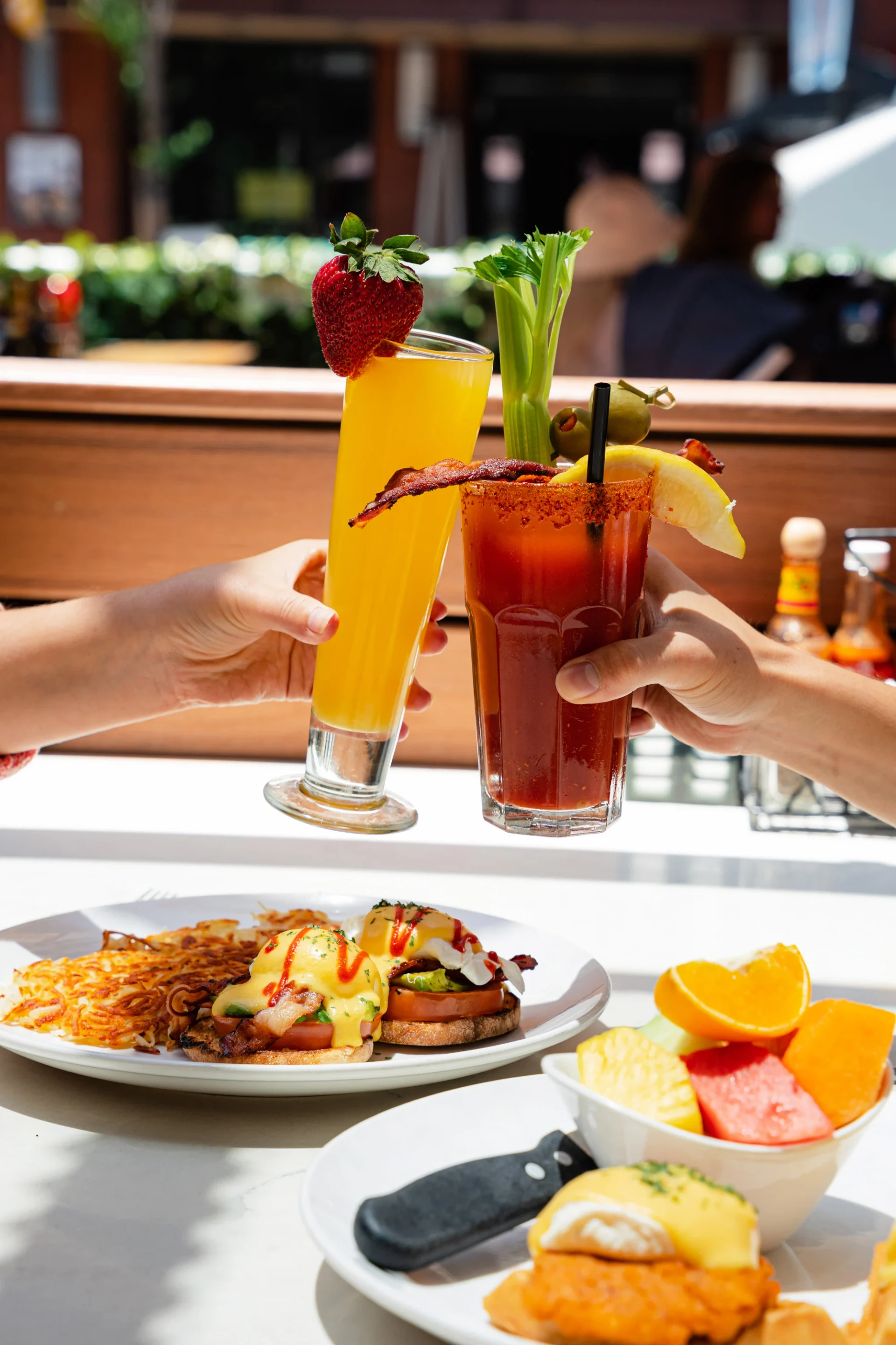 People cheers with a mimosa and Bloody Mary over breakfast Benedicts at Broken Yolk.
