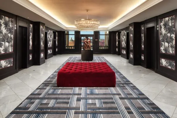 The elevator bank with red ottoman and chandelier.