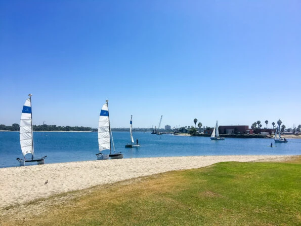 A small beach with little catamaran sail boats on a sunny day.